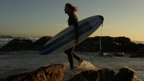Surfer walking through the rocks to get to the ocean Stock Footage 340214109