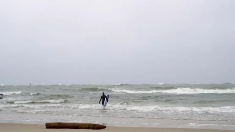Surfer in wetsuit trying to catch a wave in a cold stormy sea on a windy day. 스톡 동영상 309011913