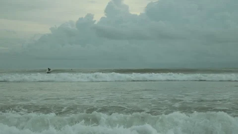 Surfers in ocean waves under cloudy sky, serene seascape, and Видео 285073764