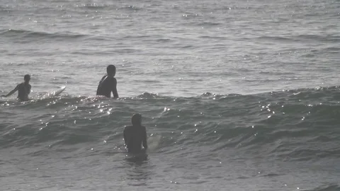 Surfers paddle out to waves at sunset. Stock Footage 82330176