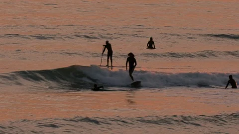 Surfers ride waves at sunset Видео 101265661