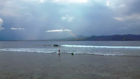 Surfers riding ocean wave under vibrant rainbow. Amazing aerial view drone Stock Footage 340199498