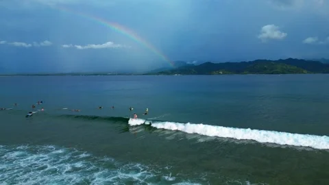 Surfers riding ocean wave under vibrant rainbow. Majestic aerial view drone Stock Footage 344589385