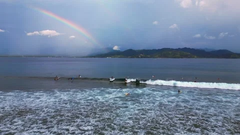 Surfers riding ocean wave under vibrant rainbow. Dramatic aerial view drone Stock Footage 344603208