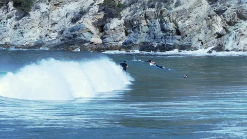 Surfers riding a wave in a day of sun near a rocky beach Stock Footage 89570892