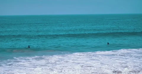 Surfers riding waves in turquoise ocean under clear sky Stock Footage 339519894