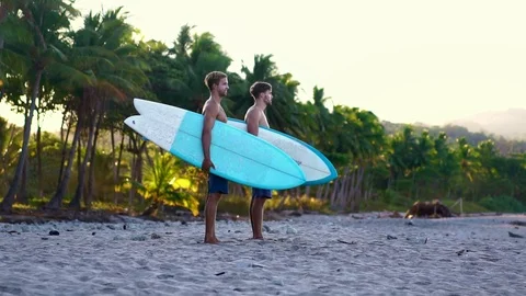 Surfers in tropical beach holding surfboards. Look at the waves in ocean.  Stock Footage 108564317