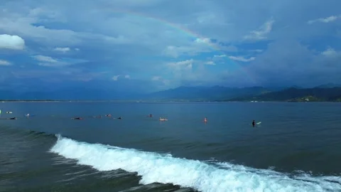Surfers waiting in ocean with rainbow over mountains. Nice aerial view drone Stock Footage 344601893