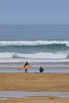 Surfers waiting for waves on sandy beach Stock Photos