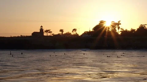 Surfers in the water at sunset with lighthouse in background Stock Footage 85918352