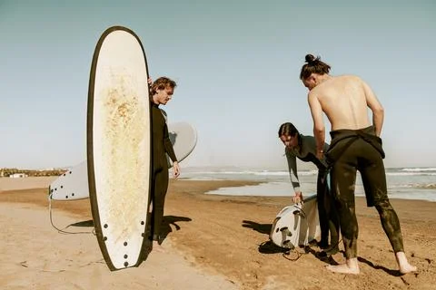 Surfers in wetsuits standing on beach with surfboards and preparing for ride on Stock Photos