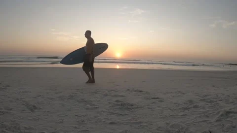 Surfist walking on the beach at sunset with his surf skate under his arm. Stock Footage 155956450