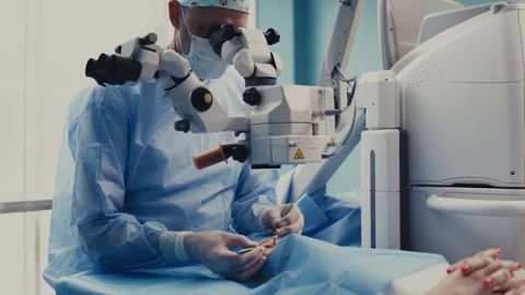 Surgeon in blue scrubs performs eye surgery using a microscope, focused on Stock Footage 337288443