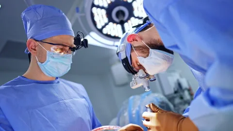 Surgeon leaned low above the patient using metal instrument.  Stock Footage 295678120