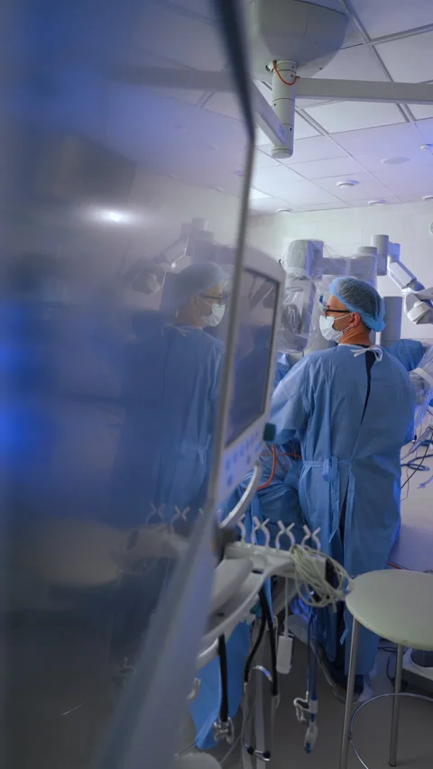 Surgeon in long blue robe stands in the operative field of Da Vinci robot.  Stock Footage 288994372