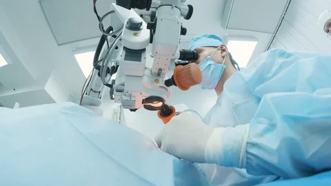 Surgeon looking into the microscope at the eye of patient at the operating room Stock Footage 129872712