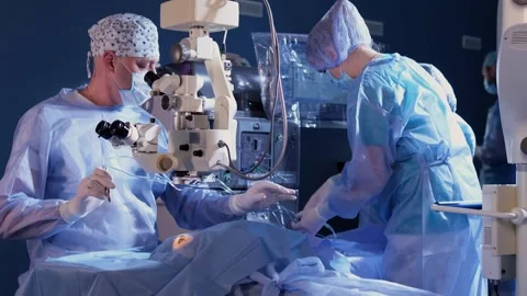 A surgeon looks through a microscope at a patient's eyes in the operating room Stock Footage 265012385