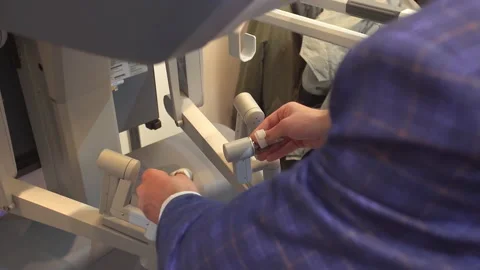 A surgeon in a plaid jacket tests the control knobs of a new medical robot 스톡 동영상 219382270