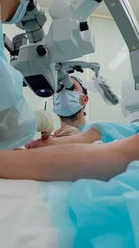 Surgeon using surgical microscope during delicate procedure over draped patient Stockfoto's