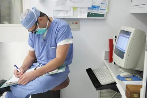 Surgeon writing in chart next to computer Stock Photos