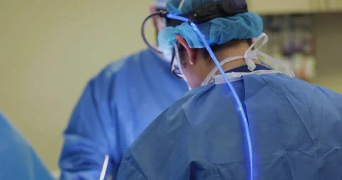 Surgeons Collaborating on a real operation with neon blue head lamp torch Stock Footage 146615820