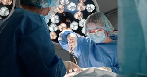 Surgeons performing complex operation under bright surgical lights Stock Footage 302716476