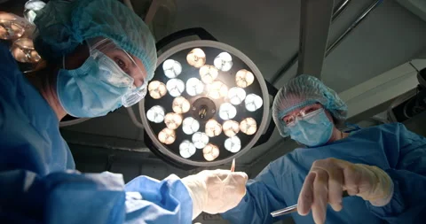 Surgeons performing operation under bright surgical lights in operating room Stock Footage 302717697