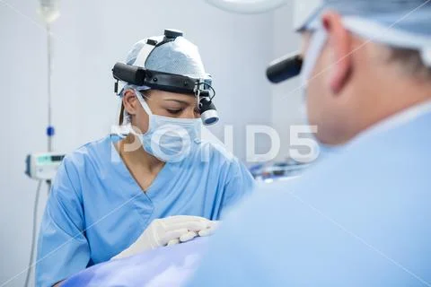 Surgeons wearing surgical loupes while operating patient Stock Photos