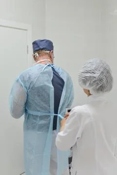Surgery, assistant helps surgeon to put on surgical clothes, back view . Stock Photos