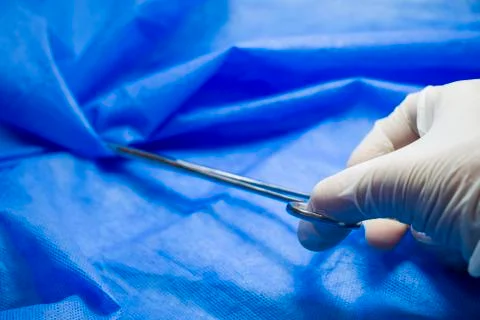 Surgery forceps in doctors hand, on the blue background, studio shoot. Operat Stock Photos