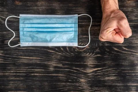 Surgical mask placed on a table and a clenched fist beside it to express Stock Photos