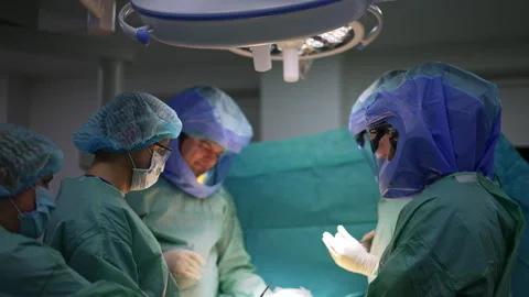 Surgical team in protective suits working under the bright lamp in surgery room. Stock Footage 241124662