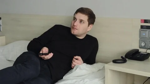 Surpised young man with TV remote watching tv on bed Stock-Footage 73450813