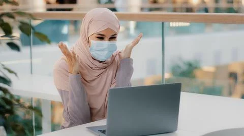 Surprised arab woman wearing medical mask looking at laptop screen receiving Stock Photos