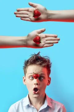 Surprised boy with a falling strawberry squinted his eyes to his nose on a bl Photos