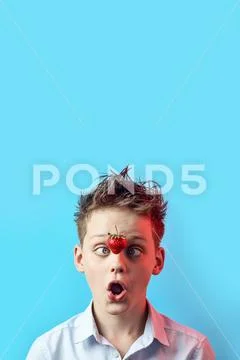 Surprised boy with a falling strawberry squinted his eyes to his nose on a bl Stock Photos