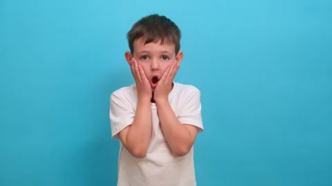 Surprised boy holding face with hand. Shocked kid with mouth open looking at Stock Footage 337426762
