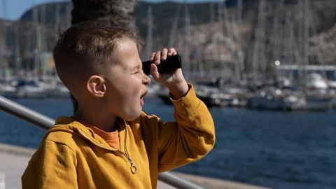 Surprised boy looking through binoculars near marina with yachts 스톡 사진