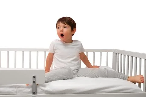 Surprised boy sitting in bed isolated on white background. Child with open mo 库存照片