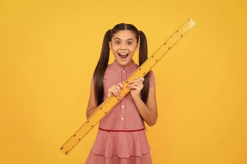 Surprised child hold school math tool ruler on yellow background, school Stock Photos