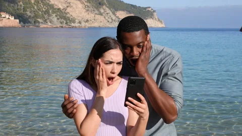 Surprised couple checking smart phone on the beach Stock Footage 170387200