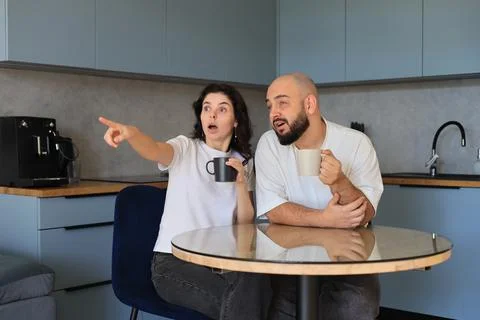 Surprised couple pointing at something while sitting at a table Stock-Fotos