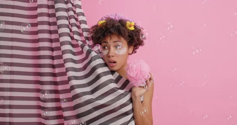 Surprised curly haired Afro American woman appears from shower curtain applies Stock Footage 147995294