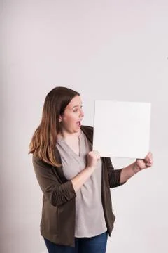 Surprised expression on woman's face looking at white blank board Stock Photos