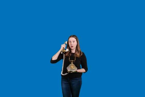 Surprised expression on womens face holding old corded phone Stock Photos