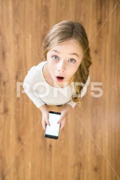 The surprised girl look up and hold a phone in hands. View from above Stock Photos