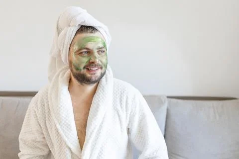Surprised guy spends hours treating and caring for his skin, applies green face Stock Photos