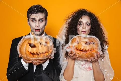 Surprised halloween bride and groom looking camera and holding pumpkin Stock Photos