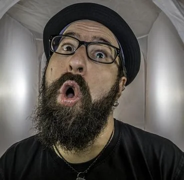 A surprised looking bearded man with black hat and glasses Stock Photos