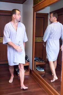 The surprised man in a bathrobe looking in the mirror at himself reflection.. Stock Photos